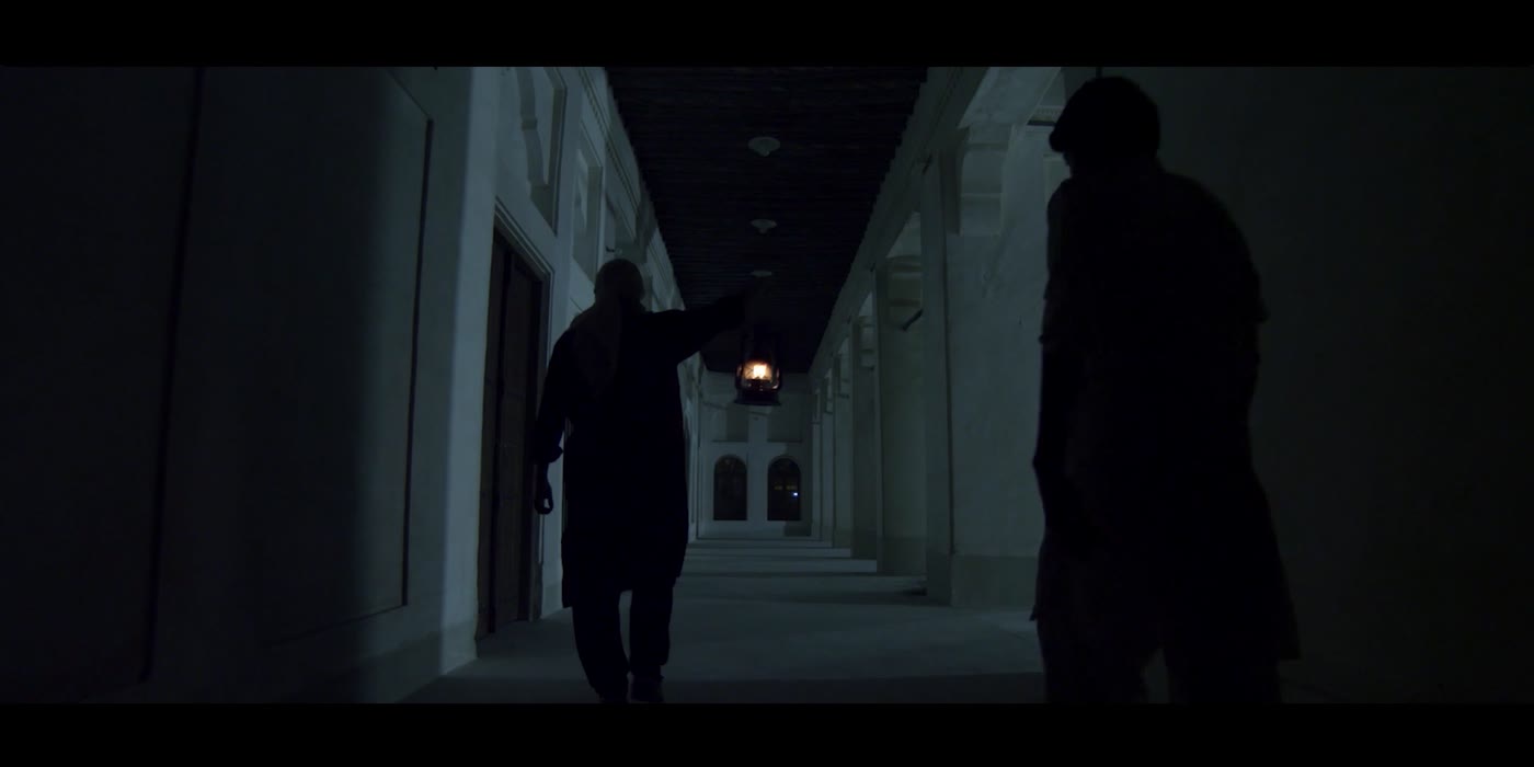 Two silhouetted figures in a long arched corridor, a lantern between them.